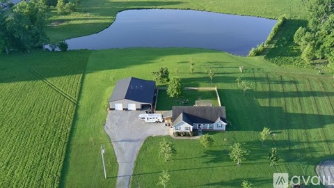 A house with a garage is situated on a grassy field next to a body of water.