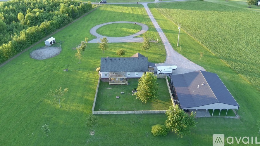 A large house with a driveway and a covered patio is surrounded by a grassy field.