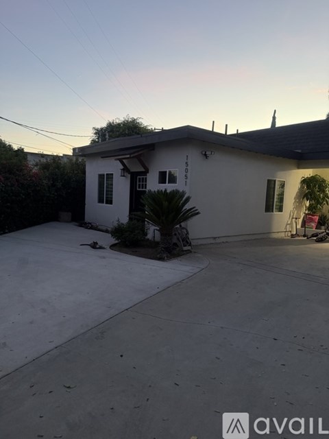 A house with a white exterior and a brown roof is shown with a driveway in front.