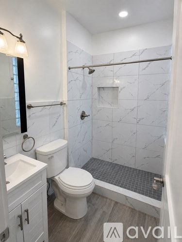 A white toilet sits in a bathroom with marble tile walls and a walk-in shower.