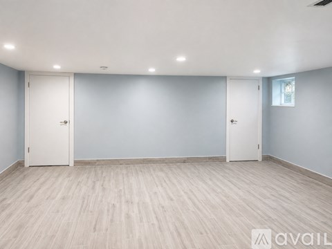 A spacious room with light wood flooring and white doors.