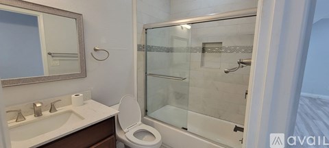 A bathroom with a toilet, sink, mirror, and shower.