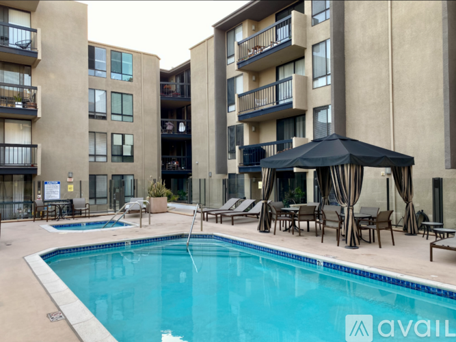A swimming pool area with a black canopy and lounge chairs in front of apartment buildings.