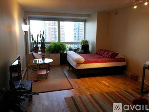 A bedroom with a bed, a table, and a window with plants.