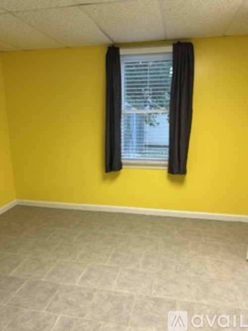 A room with a yellow wall and a window with black curtains.