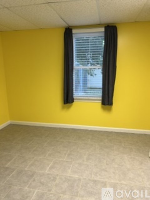 A room with a yellow wall and a window with black curtains.