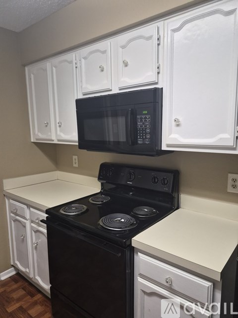 A black microwave is mounted above a black stove in a kitchen with white cabinets.