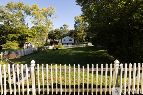 A white picket fence in front of a green lawn and trees.