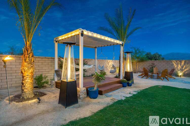 A patio area with a gazebo, palm trees, and a lit pathway.