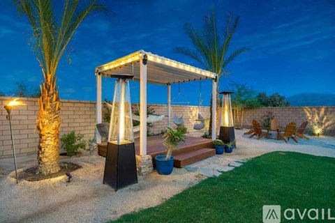 A patio area with a gazebo, palm trees, and a lit pathway.