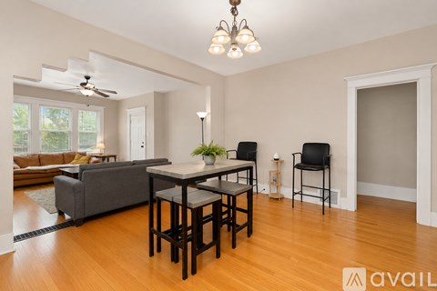 A living room with a grey couch, a table with two chairs and a plant on it.