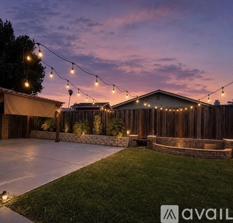 A backyard with a patio, string lights, and a house.