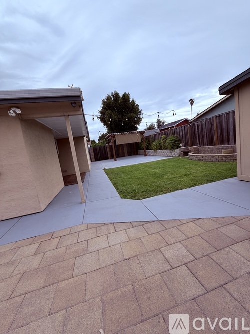 A backyard with a paved walkway and a fence.