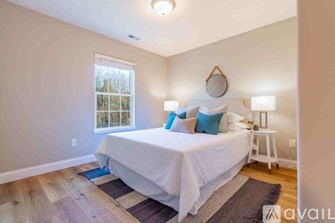 A bedroom with a white bed and a window with a view of trees.