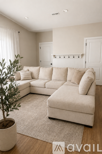 A living room with a white couch and a plant in a white pot.