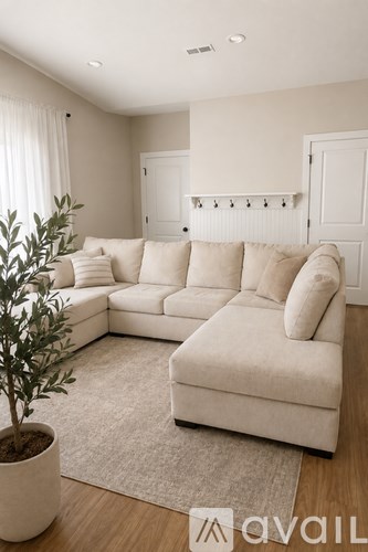 A living room with a white couch and a plant in a white pot.