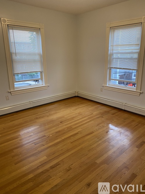 A room with wooden flooring and two windows.