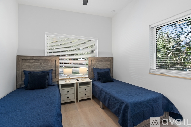 Two beds with blue bedspreads in a room with a window showing trees outside.
