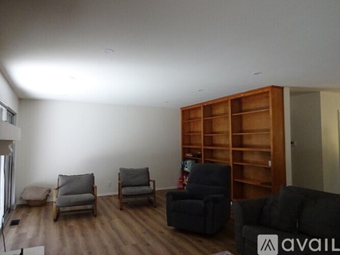 A living room with a grey couch, two chairs and a bookshelf.