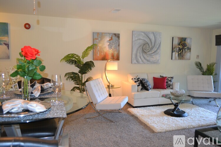 A living room with a glass table, white couch, and a red rose.