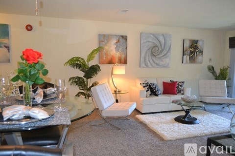A living room with a glass table, white couch, and a red rose.