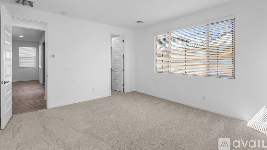 A spacious room with a door, a window with blinds, and a carpeted floor.