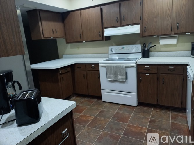 A kitchen with a black fridge, white stove, and wooden cabinets.