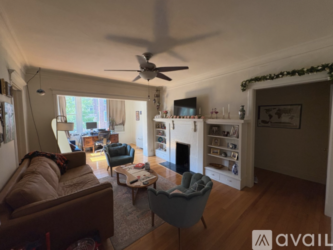 A living room with a brown leather couch, a grey armchair, a wooden coffee table, a fireplace, and a ceiling fan.