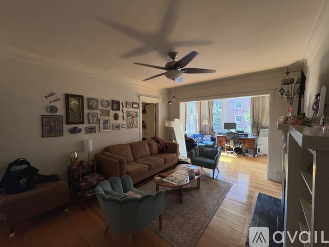 A living room with a brown couch, a blue armchair, and a ceiling fan.