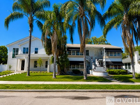 A white two-story house with a balcony on the second floor is surrounded by palm trees.