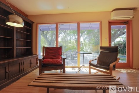 A living room with a red chair and a black chair facing a glass door.
