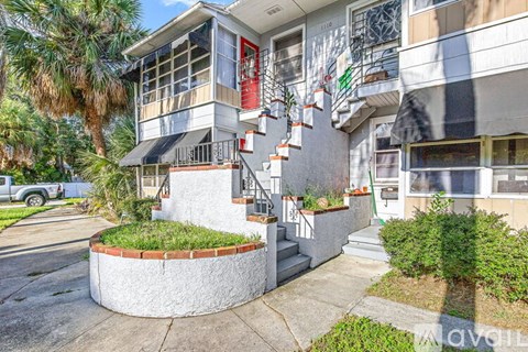 A multi-story building with a red door and a circular garden in front.