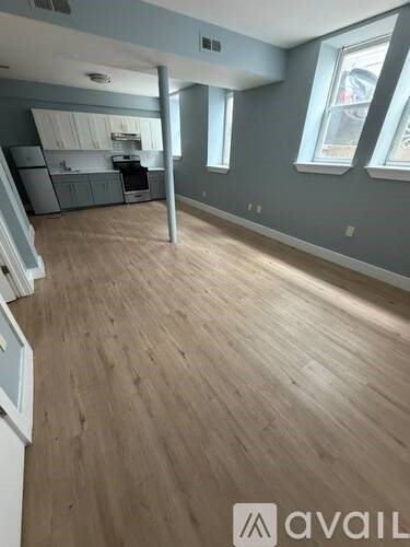 A spacious room with wooden flooring and a kitchen area in the background.