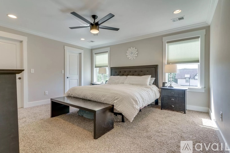 A bedroom with a bed, nightstand, and a table with a fan on the ceiling.