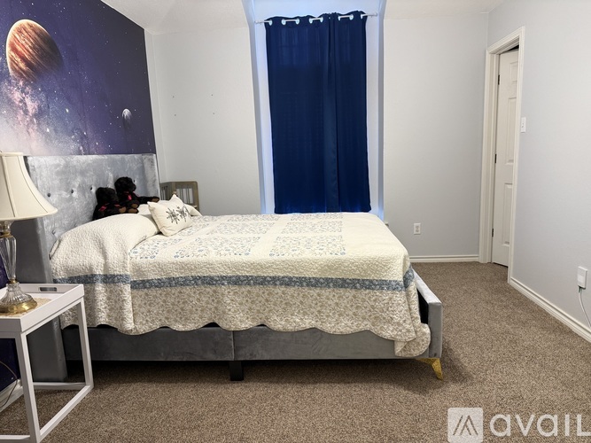 A bedroom with a bed, a nightstand with a lamp, and a wall mural of a planet.