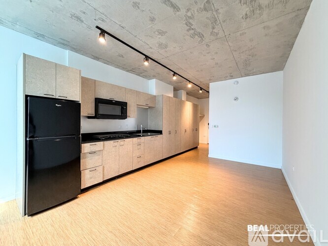 A kitchen with a black fridge and microwave, wooden floors, and a white wall.