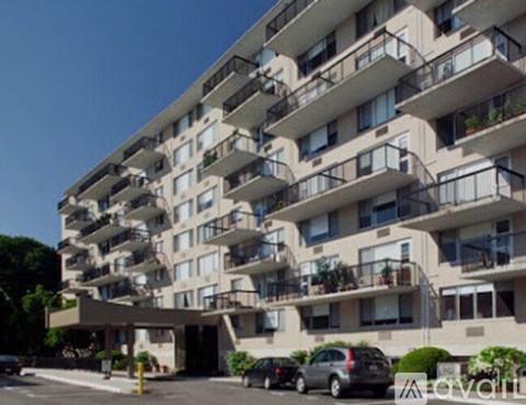 Apartment building with balconies and cars parked in front.