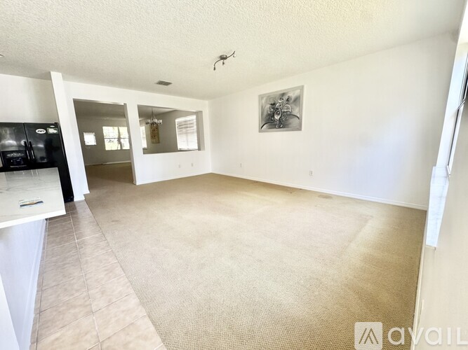 A spacious living room with a beige carpet and a framed picture on the wall.