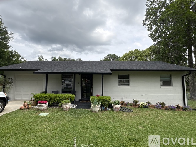 A house with a black roof and white walls is surrounded by a garden with various plants and flowers.