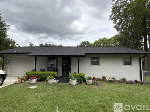 A house with a black roof and white walls is surrounded by a garden with various plants and flowers.