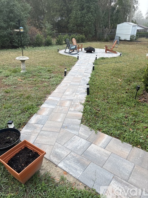A stone pathway leads from the foreground to a backyard with a patio and a tree.