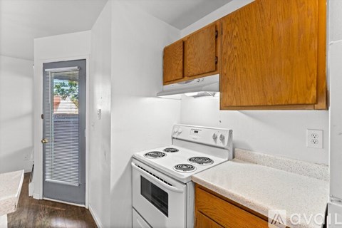 A small kitchen with a white stove top oven and wooden cabinets.