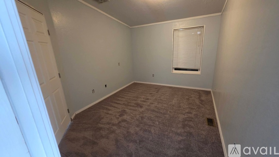 A room with a carpeted floor and a window with blinds.