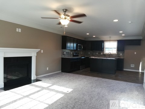 A spacious living room with a fireplace and a kitchen area in the background.