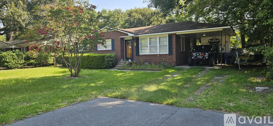 A house with a red brick exterior and a brown door is surrounded by greenery.