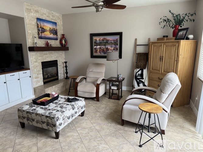 A living room with a fireplace, a chair, a table, and a painting on the wall.