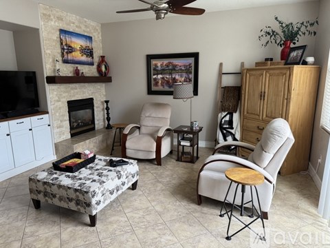 A living room with a fireplace, a chair, a table, and a painting on the wall.