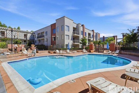 A swimming pool surrounded by lounge chairs in front of apartment buildings.