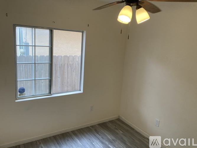 A room with a ceiling fan and a window overlooking a fence.