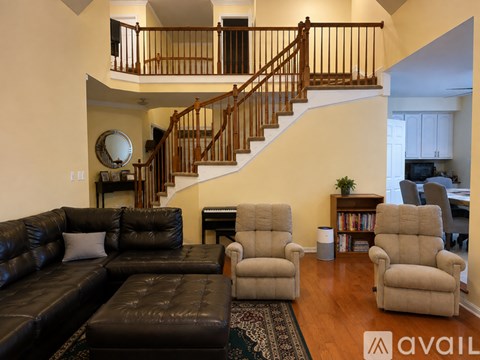 A living room with a black leather couch and a wooden staircase.
